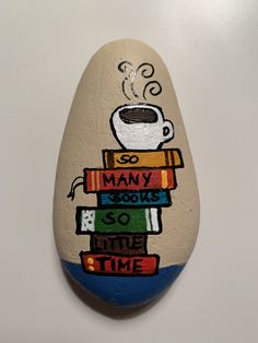 a painted rock with a coffee cup on top of books and the words many books so time to read