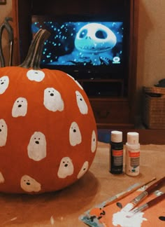 an orange pumpkin with ghost faces painted on it and paintbrushes next to it