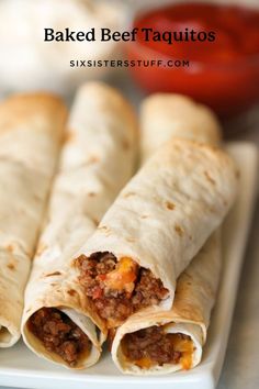 three burritos on a plate with sauce and ketchup in the background