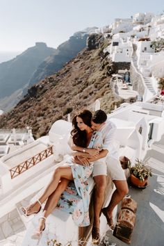 two people hugging each other while sitting on a bench in front of the ocean and mountains