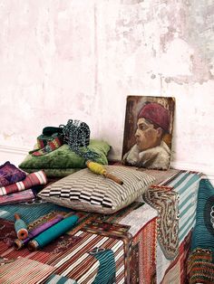 a table topped with lots of different colored pillows and blankets next to a painting on the wall