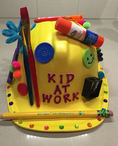 a birthday cake that says kid at work on top of a yellow plate with crayons and pencils