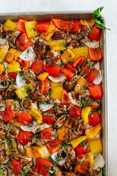 a pan filled with meat and vegetables on top of a white countertop next to green leaves