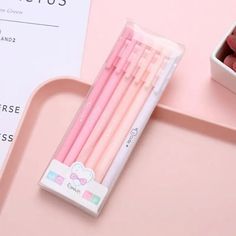 four pink pencils sitting on top of a table next to a box of chocolate candies