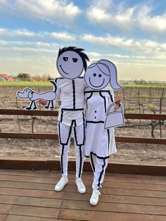 two people dressed in paper cutouts standing next to each other on a wooden deck