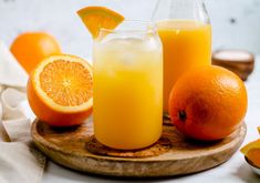 an orange juice is sitting on a wooden tray next to sliced oranges and a pitcher