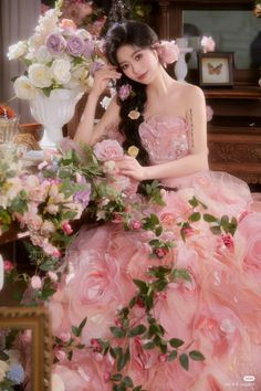 a woman in a pink dress sitting on a table with flowers