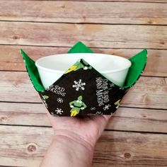 a hand is holding an origami bowl in front of a wooden table