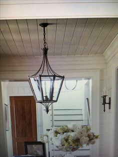 a lamp hanging from the ceiling over a table with flowers on it and a vase filled with white flowers