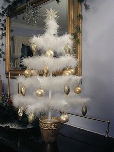 a white christmas tree decorated with ornaments and lights in front of a mirror on a table