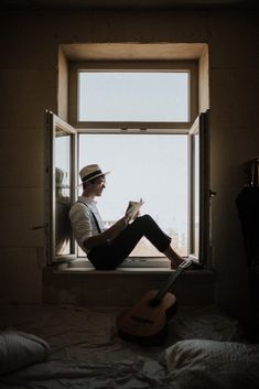 a man sitting on a window sill reading a book