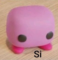 a pink toy with black eyes sitting on top of a wooden table next to the word si