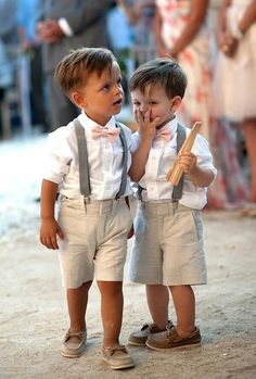 two young boys standing next to each other on a dirt road with people in the background