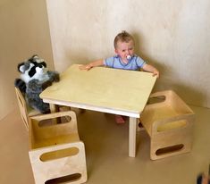 a baby sitting at a wooden table with two stuffed animals on the floor next to it