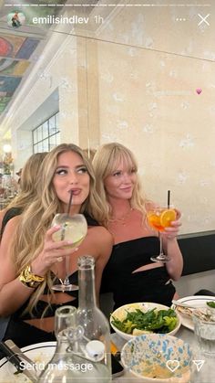 two women sitting at a table with drinks in their hands and plates on the table