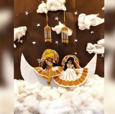 two figurines sitting on top of a moon in the middle of some clouds