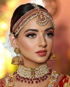 a woman in a red and gold bridal outfit with jewelry on her head, looking at the camera