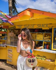 a woman standing in front of a food stand talking on a cell phone and holding a straw bag