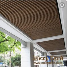 an outdoor covered porch with wood slats on the ceiling and white columns, along with trees in the background