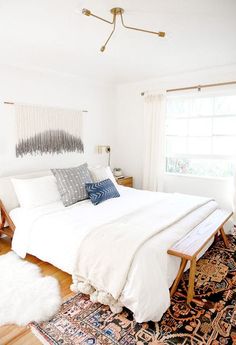 a white bed sitting in a bedroom on top of a wooden floor next to a window