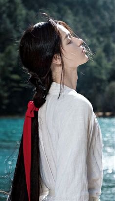 a woman with long black hair wearing a white shirt and red ribbon around her neck