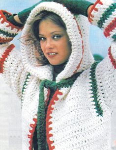 a woman is wearing a crocheted hooded sweater and green scarf while posing for the camera