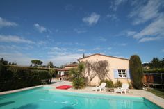 an empty swimming pool in front of a house with lawn chairs and trees around it