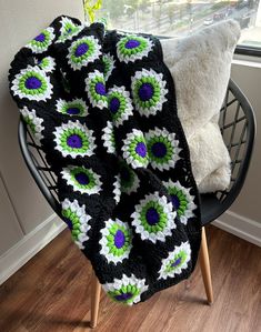 a crocheted blanket sitting on top of a chair next to a white pillow