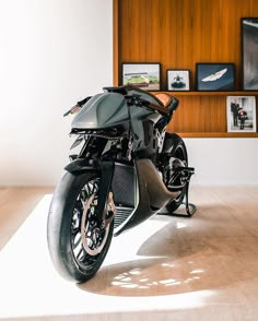 a black motorcycle parked in front of a wooden wall with pictures on the wall behind it