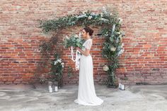 a woman standing in front of a brick wall with greenery and flowers on it