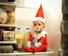 a baby in an elf costume sitting on top of a refrigerator with milk and yogurt