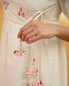 a woman wearing a white dress with flowers on it's waist and tie around her waist