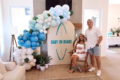 a man and woman standing next to a baby on board sign with balloons in the background