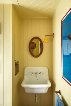 a white sink sitting under a bathroom mirror next to a wall mounted art piece and framed pictures