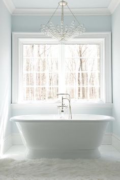 a white bath tub sitting under a window next to a rug on top of a floor