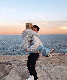 a man carrying a woman on his back while standing on the rocks by the ocean