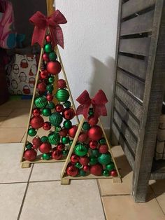 two wooden christmas trees sitting on top of a tile floor next to each other with red and green ornaments