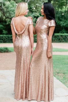 two women in gold sequin gowns looking at each other while standing on the sidewalk