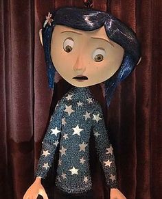 a doll with blue hair and stars on it's body is standing in front of a curtain