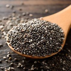 a wooden spoon filled with chia seeds on top of a wood table next to a pile of chia seeds