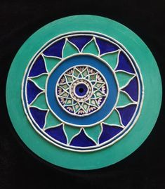 a blue and green plate with an intricate design on the front, against a black background