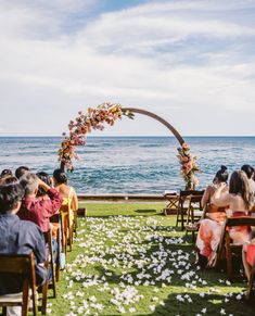 a wedding ceremony on the lawn by the ocean with an arch decorated with flowers and greenery