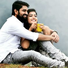 a man and woman sitting on the ground with coffee in their hands, smiling at each other