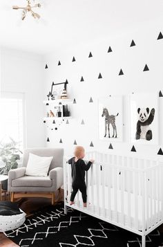 a little boy standing next to a white crib with black and white wallpaper