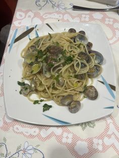 a plate of pasta with clams and parsley on a tableclothed cloth