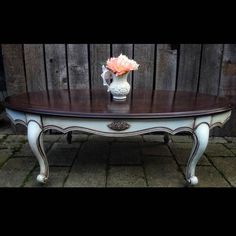 a white vase with pink flowers on top of a table in front of a wooden fence