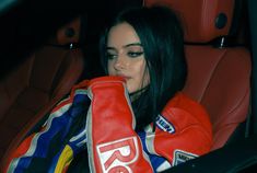 a woman sitting in the back seat of a car wearing red boxing gloves and holding her hand to her face