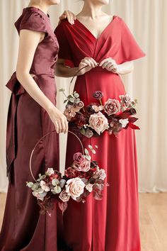 two women in red dresses standing next to each other with flowers on the back of their dresses