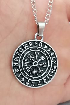 a hand holding a silver necklace with an ancient compass pendant on it's chain