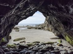 an open cave on the beach with rocks and water